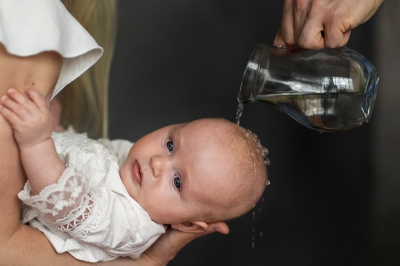 Ein Baby schaut nach vorne während bei der Taufe liegend etwa Wasser übr den Kopf gegossen bekommt